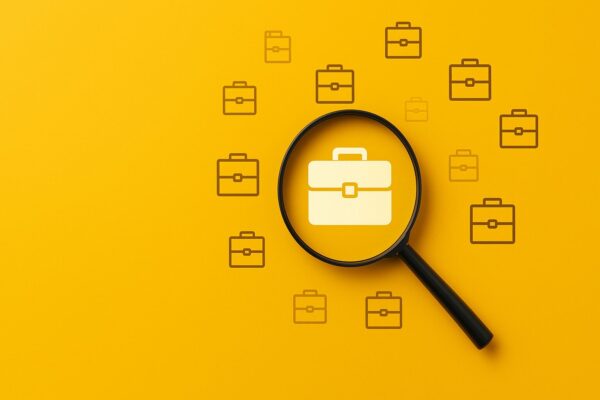 Job search concept with a magnifying glass focusing on a briefcase icon against a bright yellow background. Represents employment, career opportunities, and recruitment.