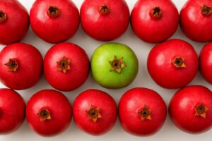 One green apple among many red pomegranates, highlighting individuality and standing out